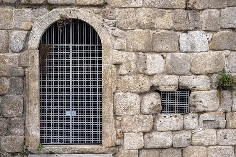 Metal grate door in rock wall, Porto, Portugal, 2019.