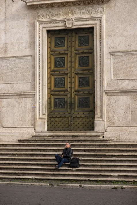 A man smokes a cigarette while sitting on steps near Piazza del Popolo in Rome, Italy, 2022.