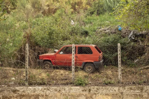 Old red Fiat Panda parked in dirt behind a fence in Rome, Italy, 2022.