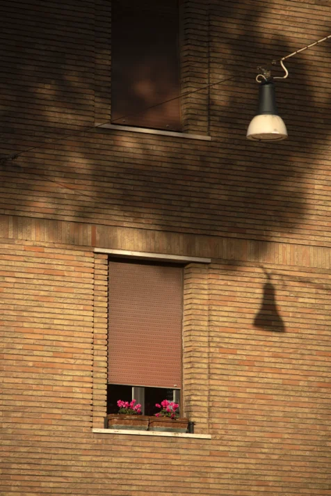 A partially-shuttered window, pink flowers and a streetlight on a sunny afternoon in Rome, Italy, 2022.