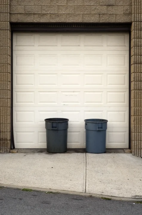 A pair of trash cans next to a garage door in Nyack, New York, 2015.