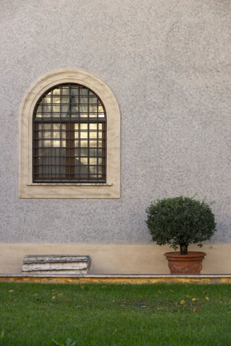 A window, potted shrub and piece of a column in Rome, Italy, 2022.
