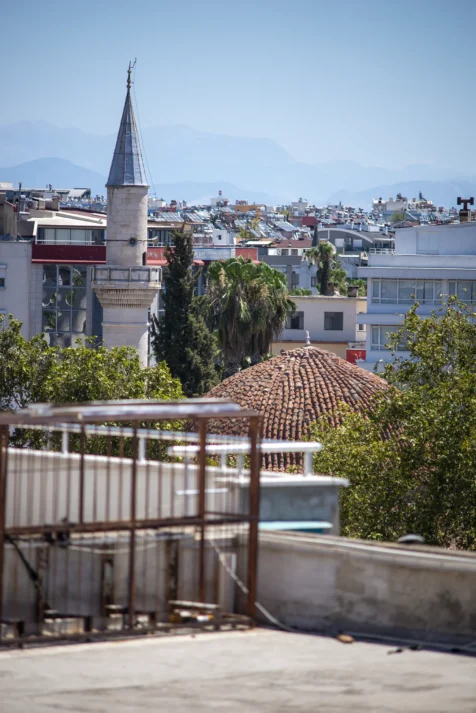 A mosque tower, assorted rooftops and mountains in the distance in Antalya, Turkey, 2024.