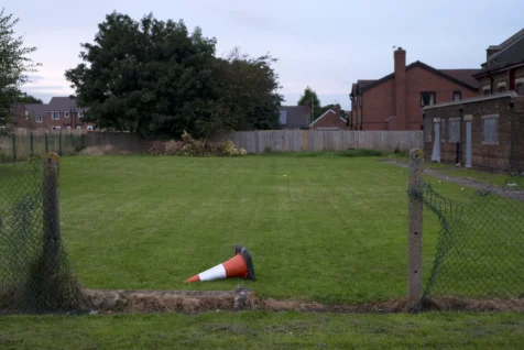 An overturned construction cone next a missing segment of chainlink fence in Warrington, England, 2017.