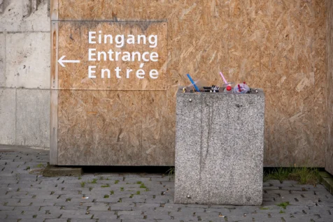 An entrance sign and full concrete trash bin near the Gothic cathedral in Ulm, Germany, 2023.