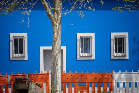 A vibrant blue building, construction barrier, tree and piece of heavy machinery in Neu-Ulm, Germany, 2023.