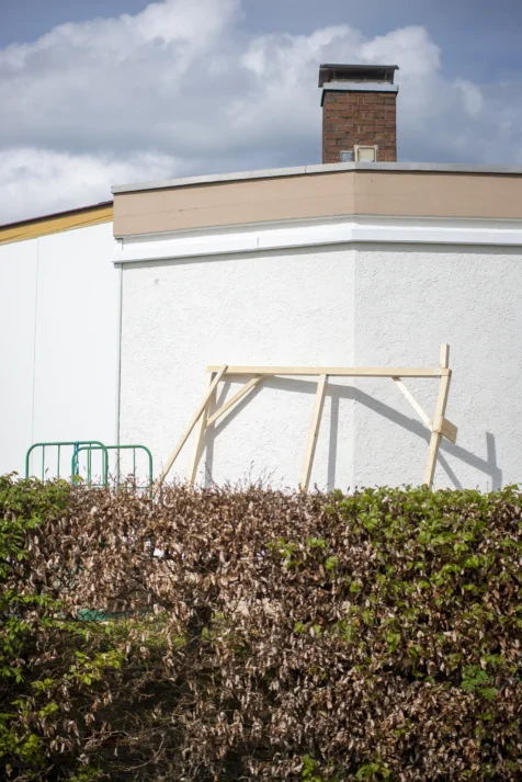 A wooden frame and metal barriers near a building behind a bush in Wiblingen, Germany, 2023.
