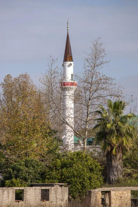A white mosque tower, trees and unfinished buildings in Antalya, Turkey, 2024.