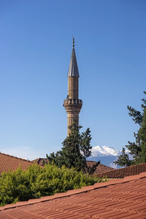 A mosque tower, trees, roofs and mountaintops in Antalya, Turkey, 2024.